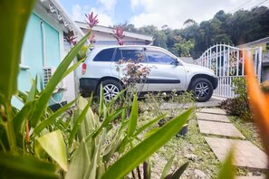 A white car parked in a driveway with a house in the background. - Peaceful Haven | 2BR | Kitchen | Parking (Roseau)
