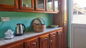 Une cuisine avec des meubles de rangement en bois, une bouilloire, un panier et un évier.