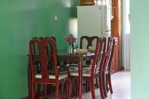 A dining area with a wooden table and chairs, a white refrigerator, and a vase with flowers.