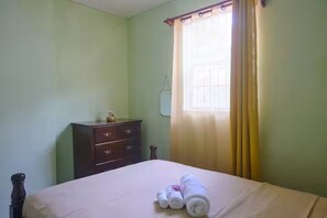 A bedroom with a bed, a dresser, and a window with curtains. - Roseau Escape | 2BR | Free Parking | Sleeps 4 (Roseau)
