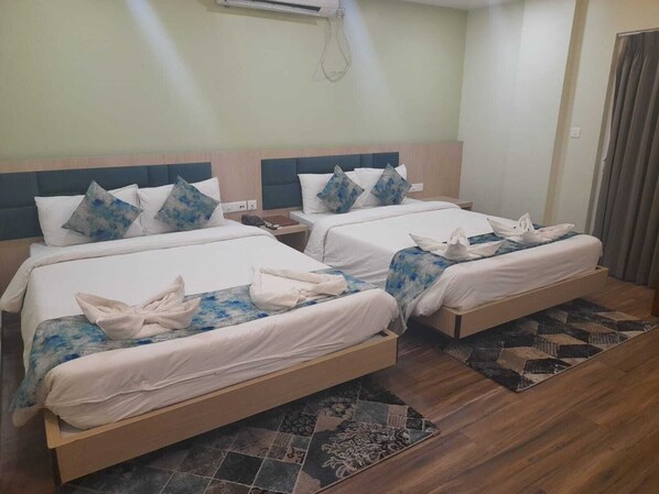 A hotel room with two beds, each with a headboard, white bedding, and blue patterned pillows. There is a wooden floor and a patterned rug.