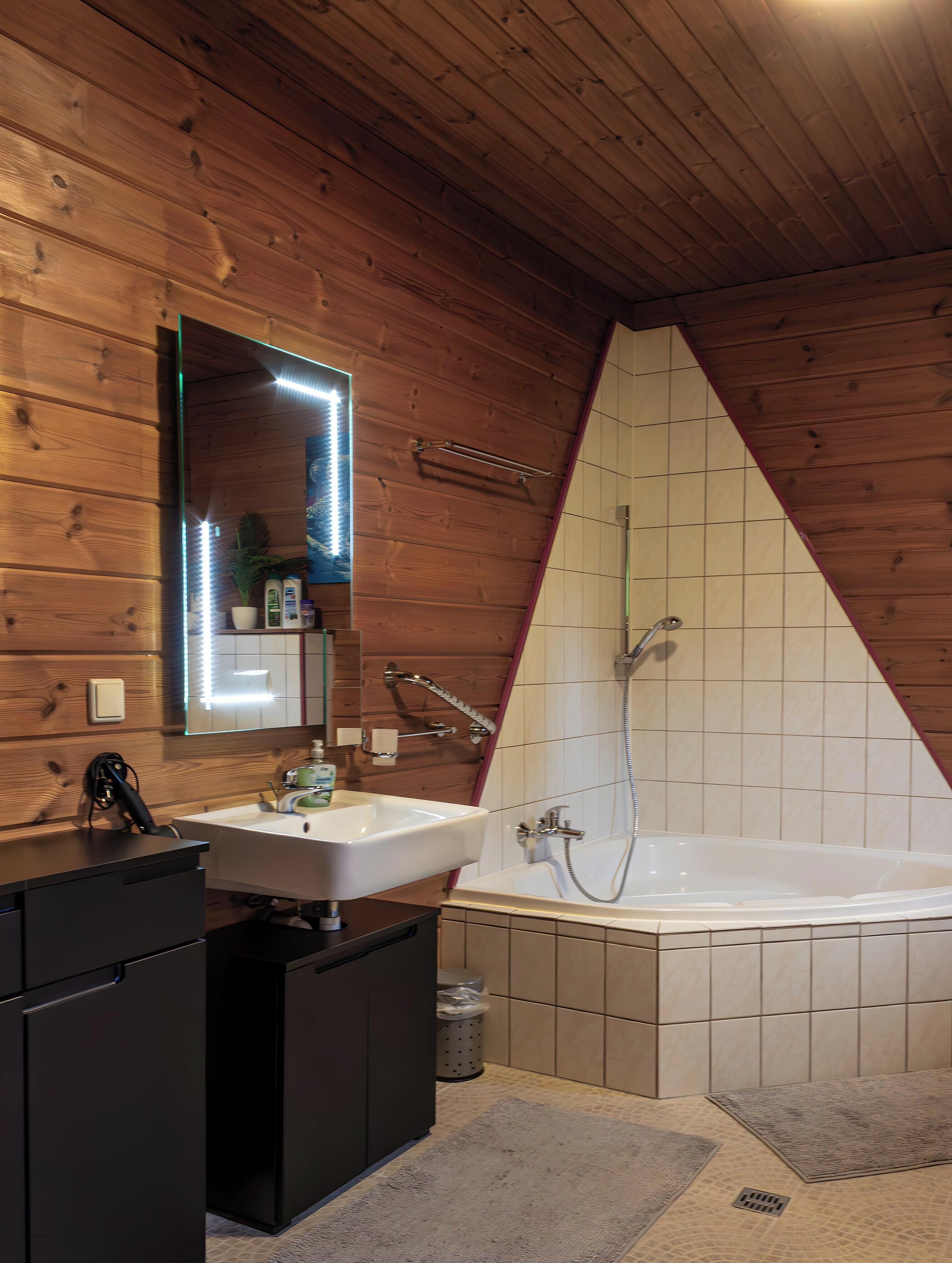 Ein Badezimmer mit Holzbalkendecke, einem weißen Waschbecken, einer Badewanne und einem Spiegel.