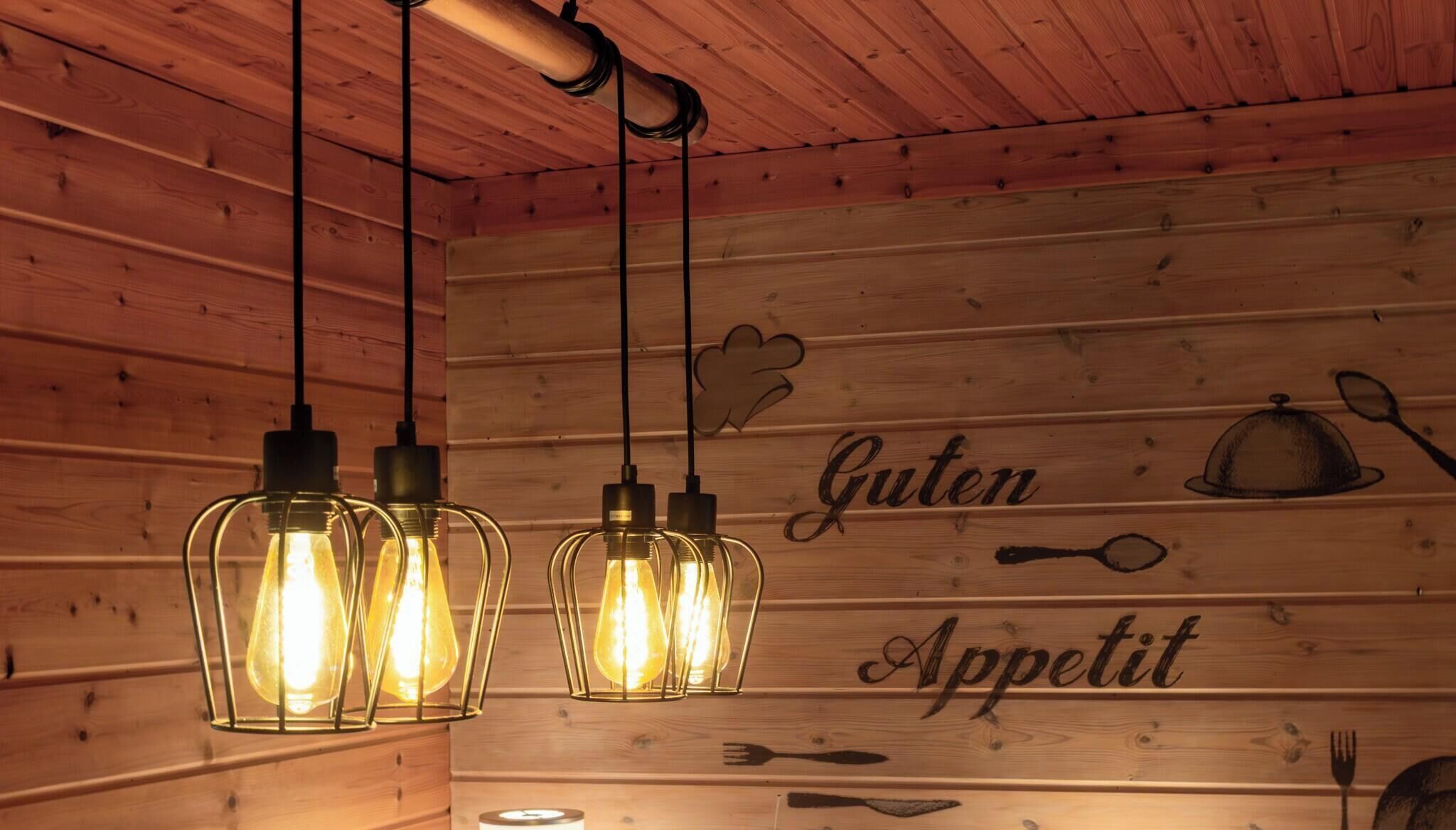 Un intérieur en bois, agrémenté de luminaires suspendus et d’un mur orné des mots « Guten Appetit » et d’illustrations sur le thème de la nourriture.