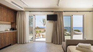 Habitació moderna amb llit, televisió, zona de cuina i una porta corredissa de vidre que dona a un pati amb vistes al mar.