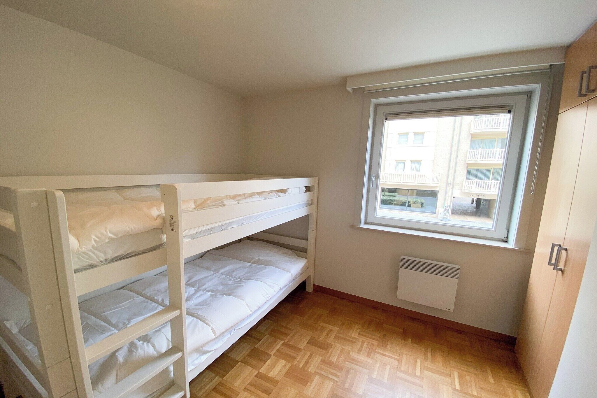 Una stanza piccola e pulita con un letto a castello, una finestra vista edifici e un termosifone.