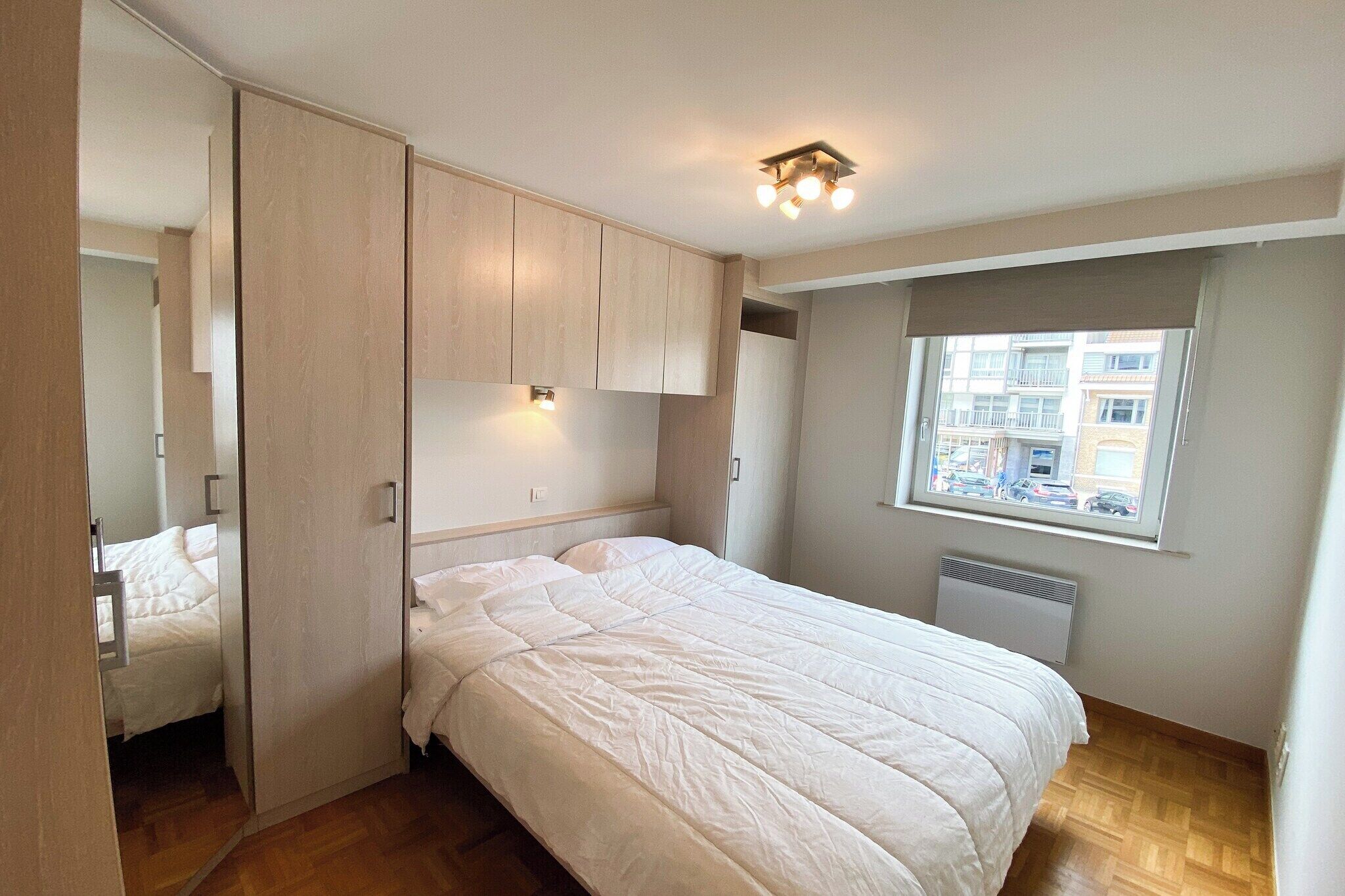Un dormitorio con cama, armario empotrado y ventana con vistas a edificios.