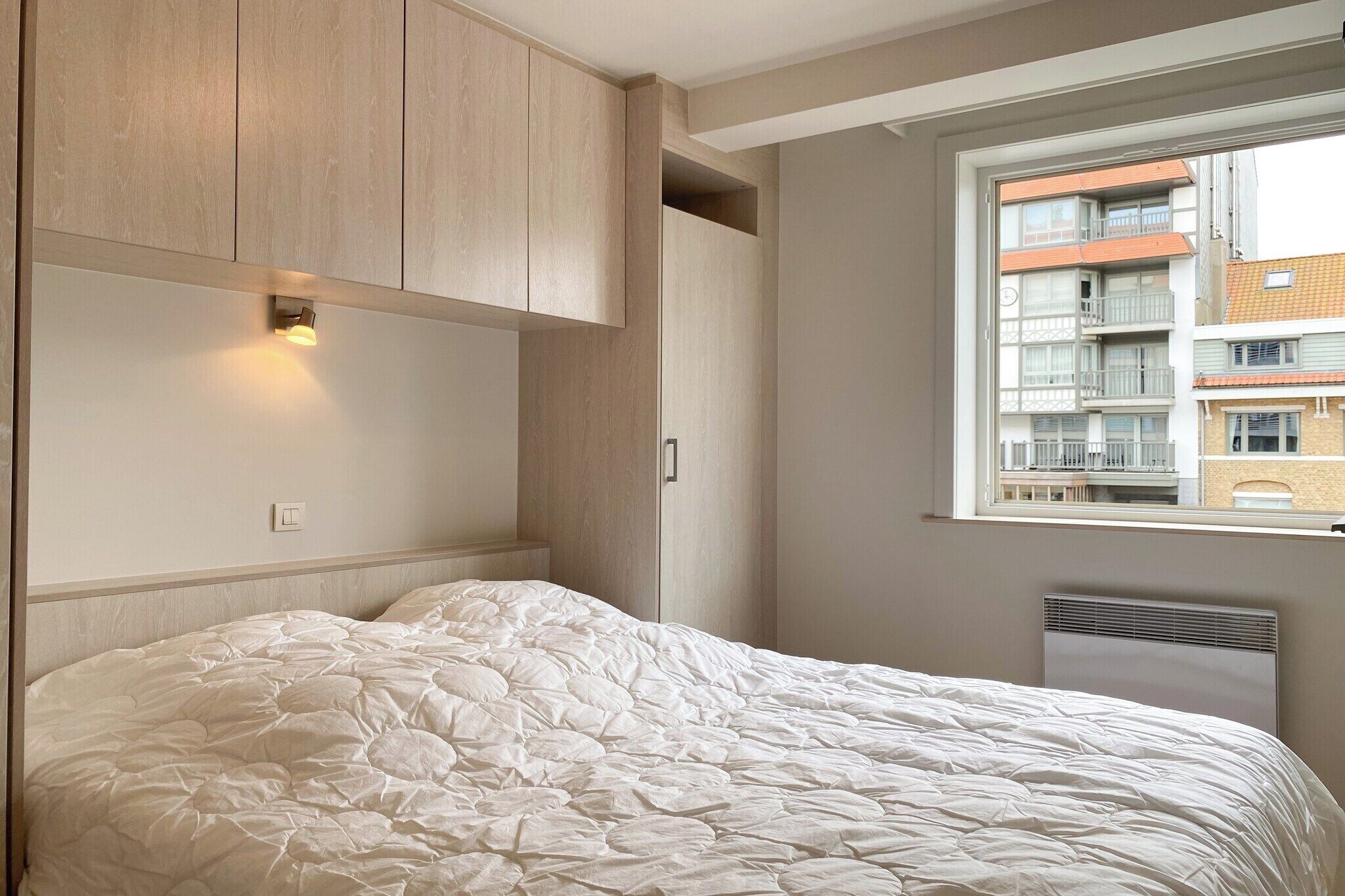 Een slaapkamer met een bed, een inbouwkast en een raam met uitzicht op gebouwen.