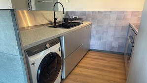 A compact kitchen with a built-in washer and dryer, stainless steel appliances, and a grey tiled backsplash. - Apartment in Nieuwpoort near Sandy Beaches (NIEUWPOORT)