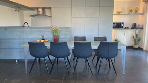 A modern kitchen with a dining area. It includes a stainless steel range hood, a built-in oven, and a microwave on a shelf. There are four chairs around a table with a vase of flowers. - Apartment in Nieuwpoort near Sandy Beaches (NIEUWPOORT)