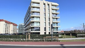 A multi-story residential building with balconies, a paved walkway, and a bench. - Apartment in Nieuwpoort near Sandy Beaches (NIEUWPOORT)