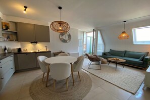 A modern kitchen with a round dining table, white chairs, and a hanging light fixture.