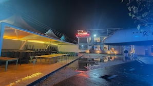 Un área de comedor al aire libre con mesas y sillas, un espacio de estar cubierto y un edificio con un letrero que dice "KOSHI AERO CLUB & RESORT".