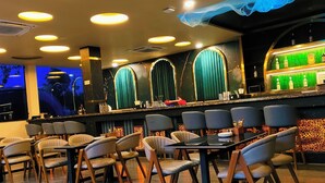 Un restaurante con zona de bar, varias mesas y sillas, y una pared iluminada en verde.