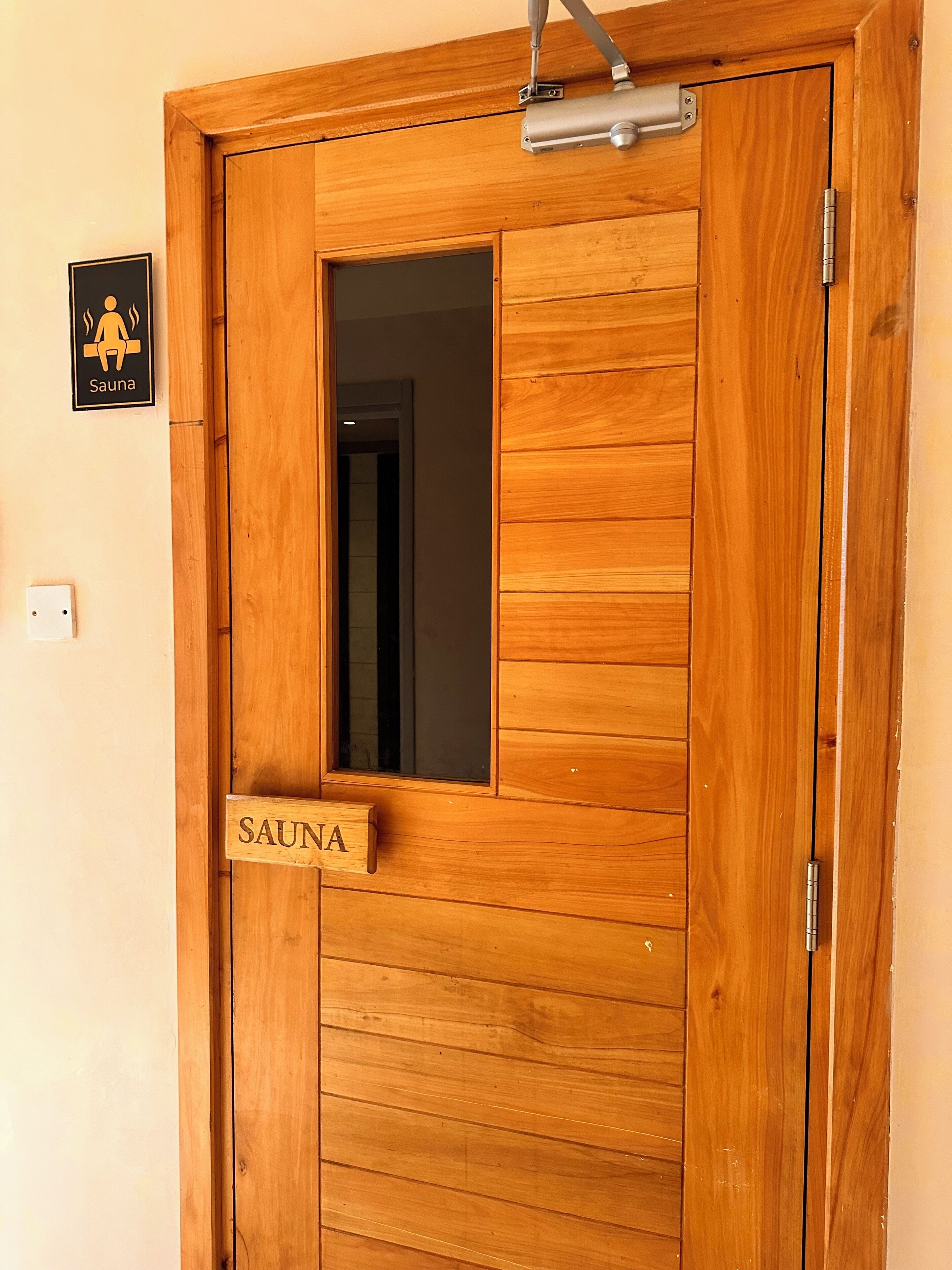 Eine Holztür mit Fenster und einem Schild, auf dem 'SAUNA' steht.