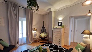 Ein Wohnzimmer mit einer Couch, einem runden Couchtisch, einem Hängekorbstuhl, einem Schrank und einer Tür.