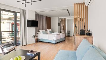 A modern hotel room with a bed, a TV, a dining area with a table and chairs, and a view of the outside.