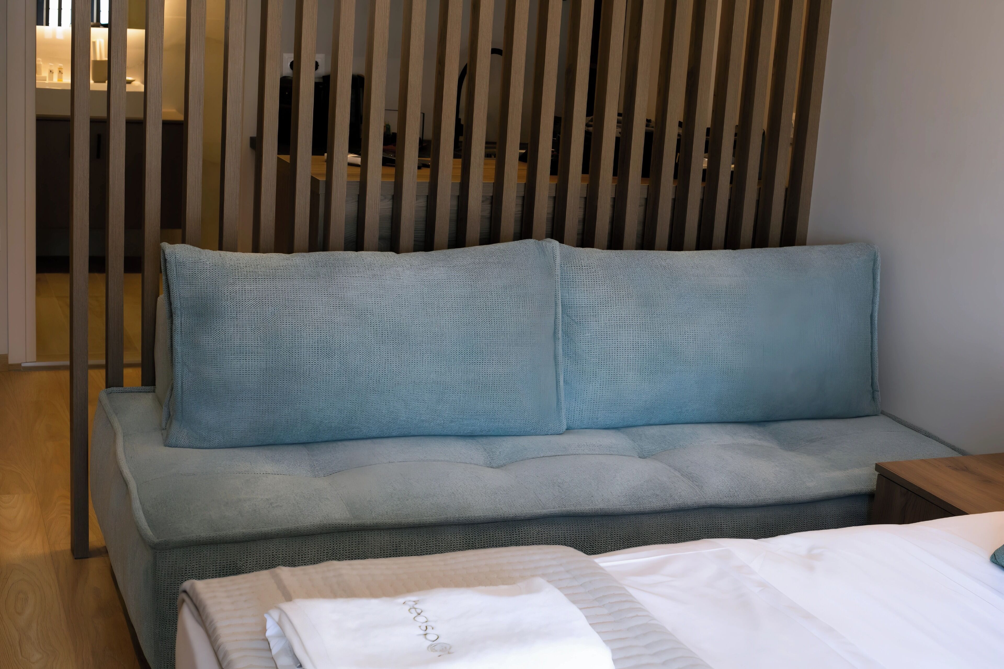 A modern room with a grey sofa, a wooden partition, and a bed with white bedding.