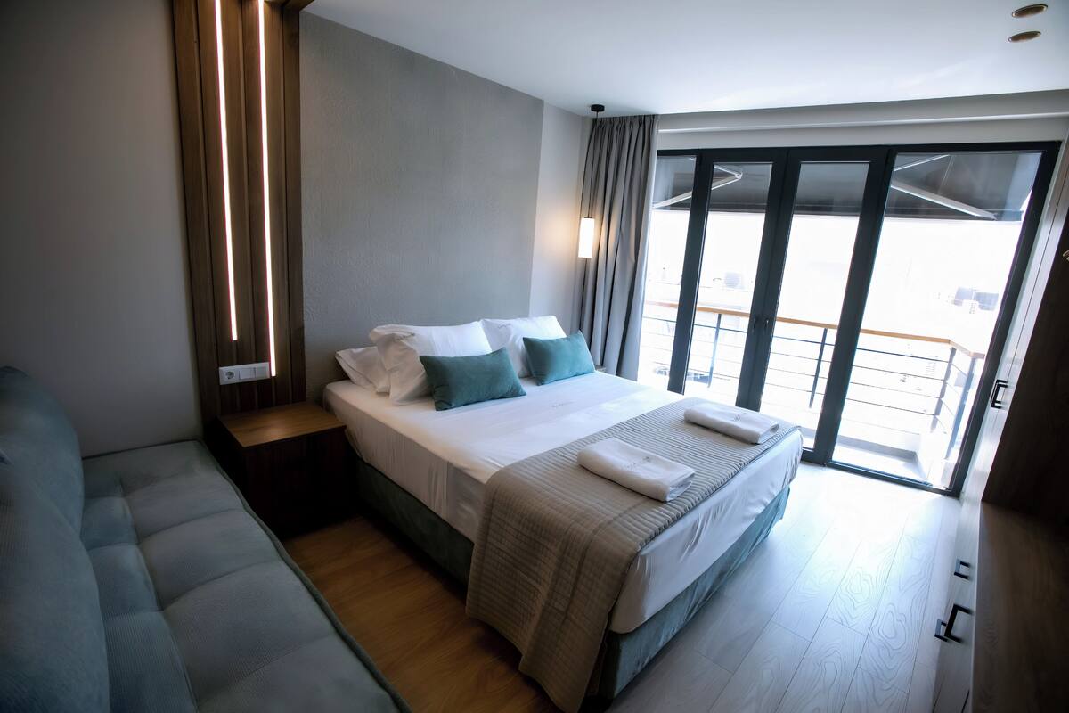 A modern hotel room with a large bed, a sofa, and a balcony with a view.