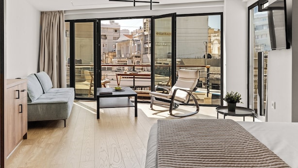 A modern hotel room with a bed, a sofa, a dining table, and a balcony with a view of the city. - Bedspot Heraklion (Heraklion)