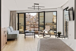 Una habitación de hotel moderna con cama, sofá, mesa de comedor y balcón con vistas a la ciudad.
