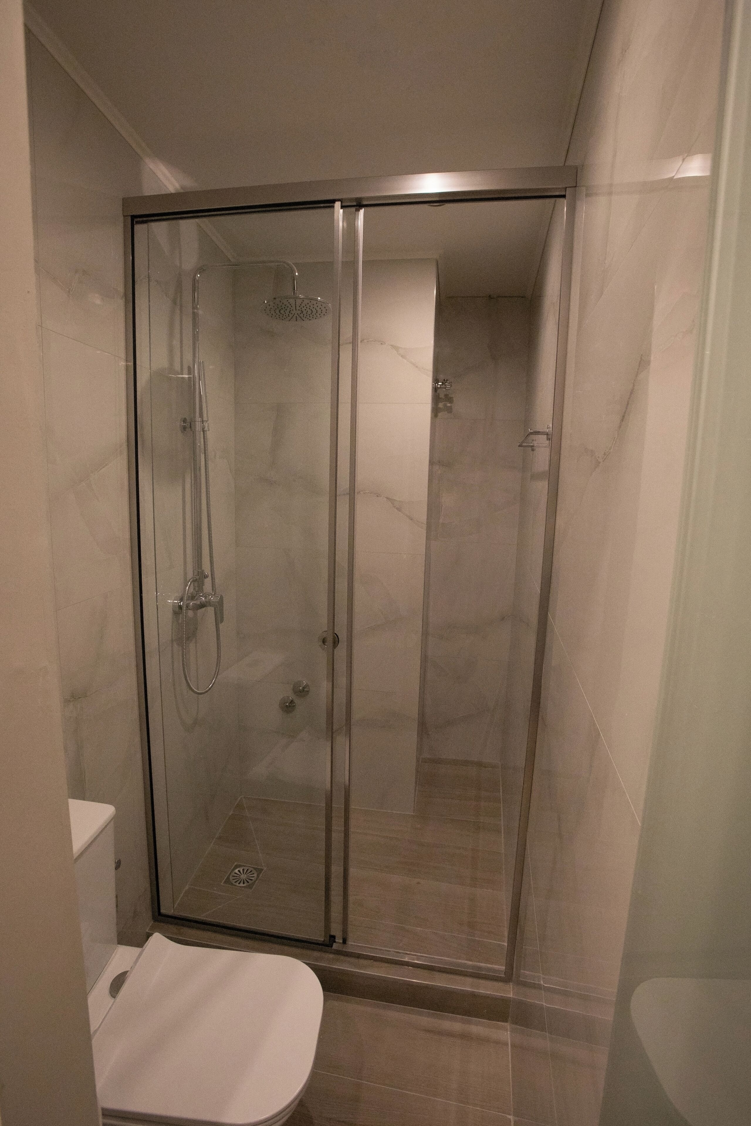 A glass-enclosed shower stall with a handheld showerhead and a wall-mounted faucet.