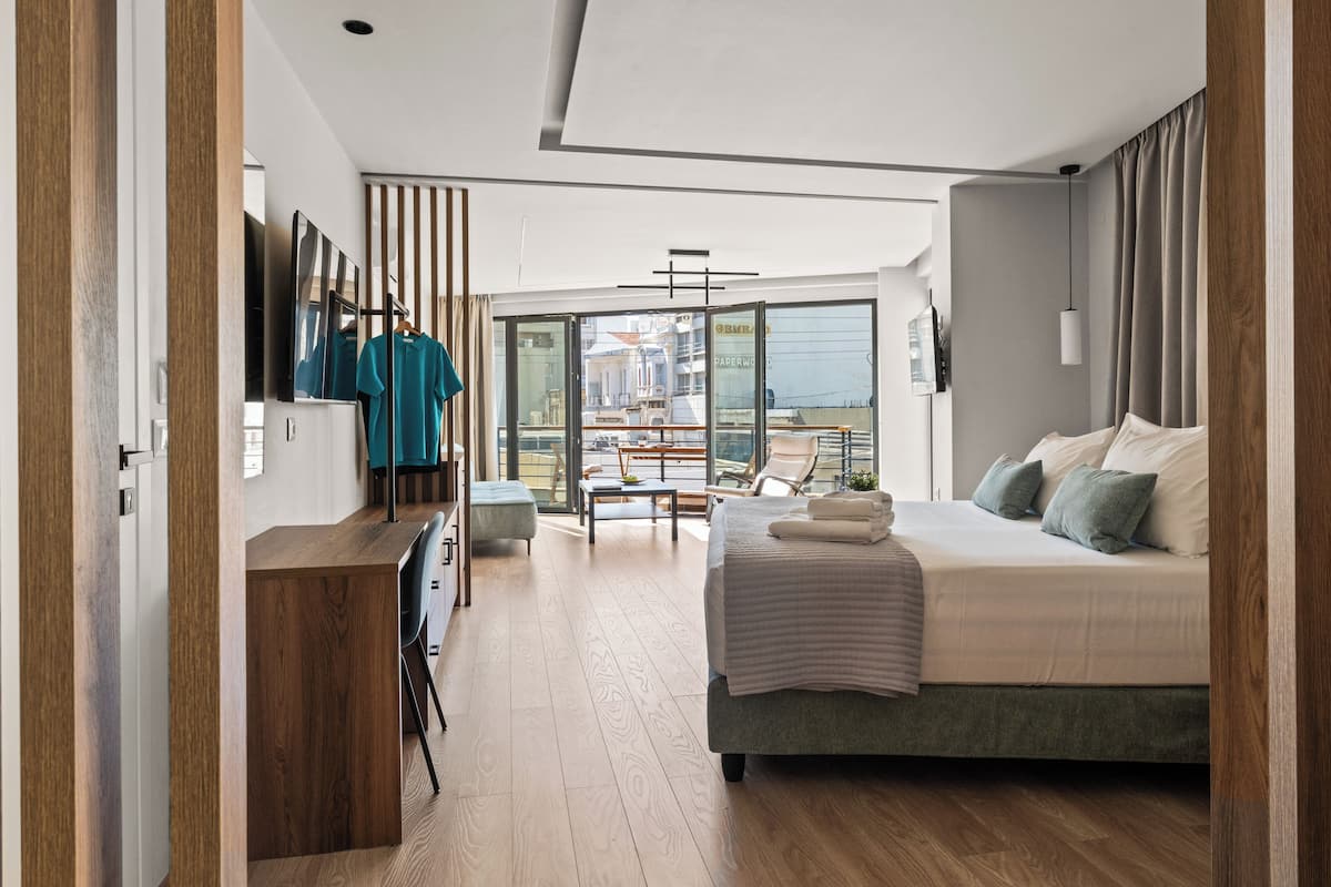 A modern bedroom with a large bed, a desk, and a balcony with a view.