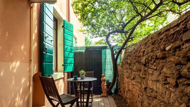 A small outdoor patio with a table and chairs, a statue, and a stone wall. - Romantic loft with private garden | Self check-in (Verona)