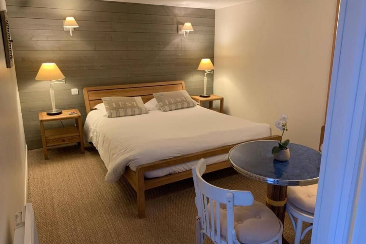 Une chambre à coucher avec un lit, deux lampes de chevet, une table ronde avec une chaise et une petite plante en pot.