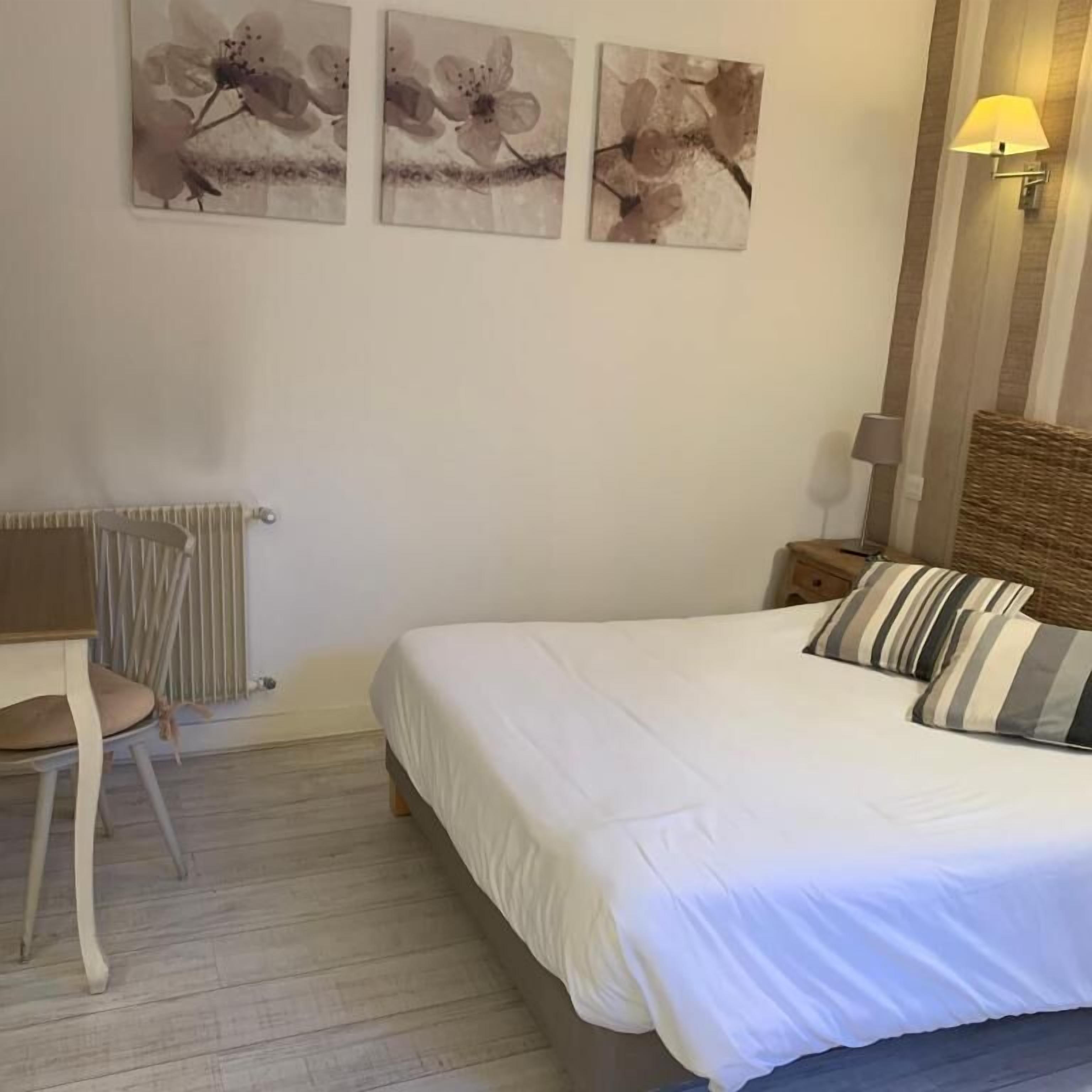 A bedroom with a bed, a chair, a lamp, and three wall-mounted flower paintings.