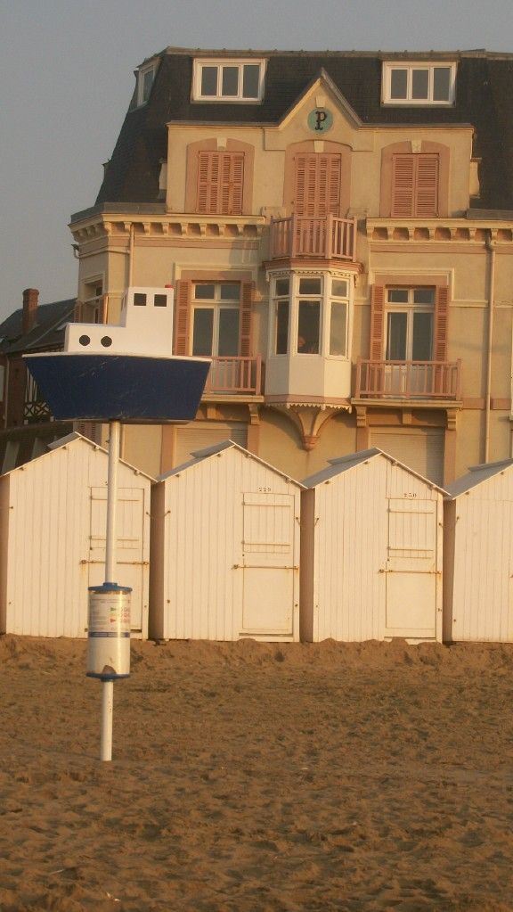 Un edificio con un balcón, un letrero con forma de barco y una fila de cabañas de playa blancas.
