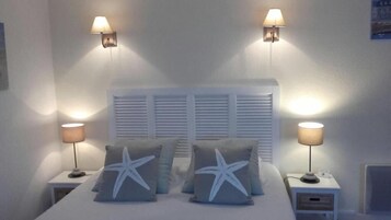 Un dormitorio con cama, dos mesitas de noche, dos lámparas de pared y una ventana con persianas.