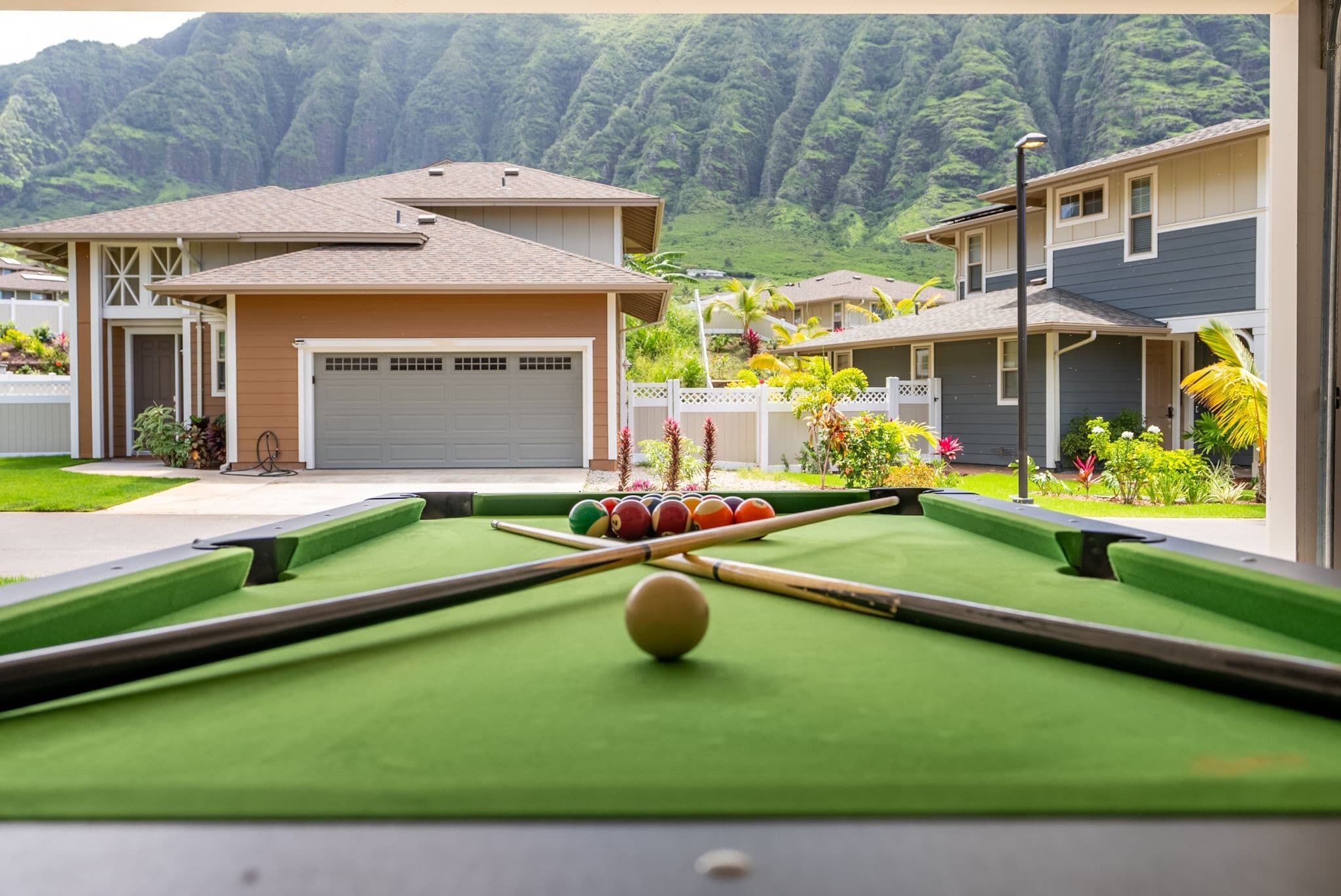 A pool table with a mountain view, surrounded by houses with a garage and a well-maintained lawn.