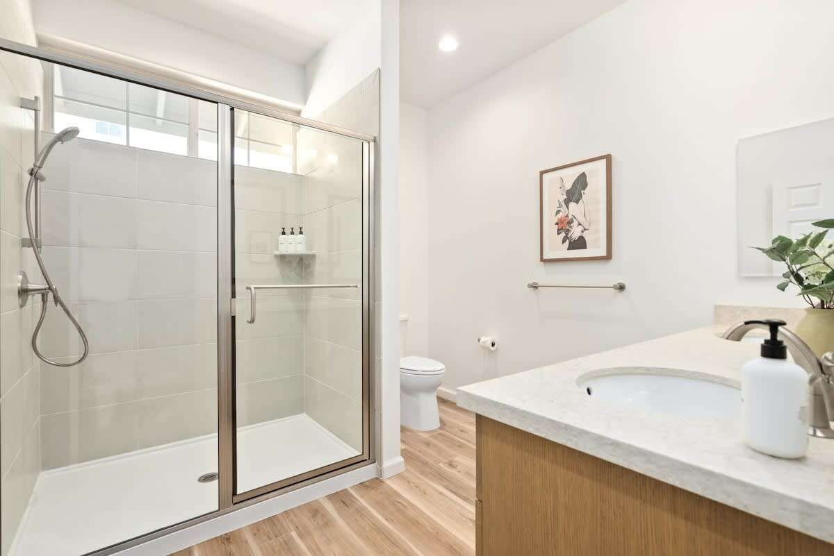 A modern bathroom with a glass-enclosed shower, a white sink with a wooden vanity, and a framed artwork on the wall.