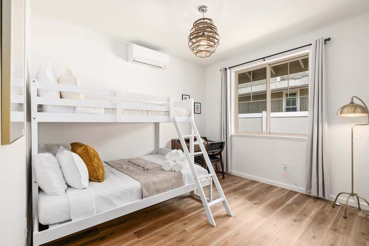A bunk bed room with a ladder, a desk, and a window with curtains.
