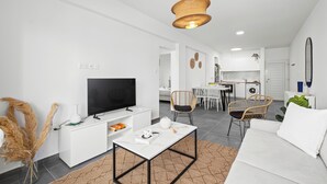 A modern living room with a white sofa, a coffee table, a TV, and a dining area with chairs.