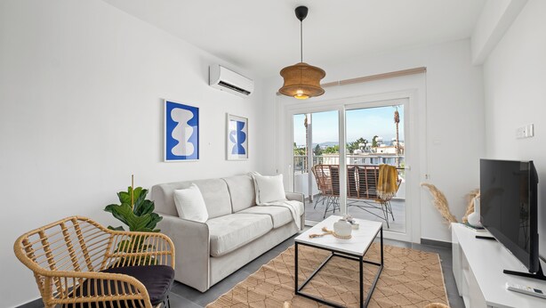 A modern living room with a sofa, two wicker chairs, a coffee table, and a TV.