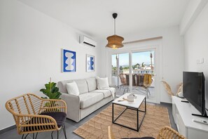 Ein modernes Wohnzimmer mit einer Couch, zwei Korbstühlen, einem Couchtisch und einem Fernseher.