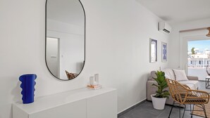 A modern living room with a white console, a large mirror, a blue vase, a potted plant, and a wicker chair.