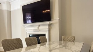 Uma sala de jantar com uma mesa de mármore, quatro cadeiras acolchoadas, uma televisão de tela plana montada acima de uma lareira e uma lareira moderna.