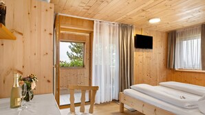 A wooden cabin room with a bed, a table with a bottle and glass, a chair, and a TV on the wall. - Room 'Bergblick' with Mountain View, Shared Garden and Wi-Fi (Sibratsgfäll)