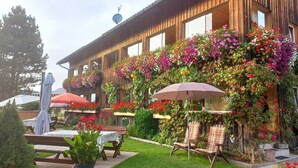 A wooden building with balconies adorned with flowers, outdoor seating, and a clear sky. - Room 'Bergblick' with Mountain View, Shared Garden and Wi-Fi (Sibratsgfäll)