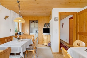 A wooden interior with a dining table, chairs, a television, and a kitchen area. - Room 'Bergblick' with Mountain View, Shared Garden and Wi-Fi (Sibratsgfäll)