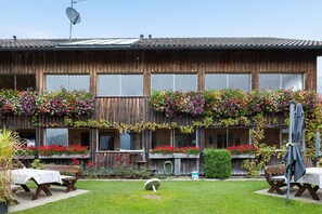 A wooden building with large windows, a balcony with flowers, and outdoor seating. - Room 'Bergblick' with Mountain View, Shared Garden and Wi-Fi (Sibratsgfäll)