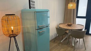 Een blauwgroene vintage koelkast, een ronde houten tafel met vier stoelen en een hoge vloerlamp met een gevlochten kap.