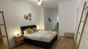 Een slaapkamer met een bed, nachtkastjes, een plafondventilator en een houten bankje.
