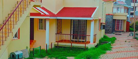 A residential area with houses featuring red roofs and yellow walls, a paved walkway, and a staircase leading to a balcony.