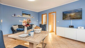 A modern living room with a dining table, a sofa, a TV, and a kitchen area.