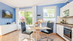 A modern kitchen with a dining area, featuring a large window, a flat-screen TV, and a built-in oven.