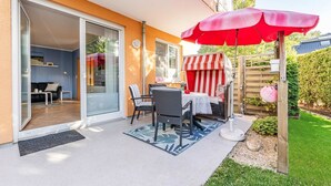 A patio with a table and chairs, a red umbrella, and a striped playhouse.