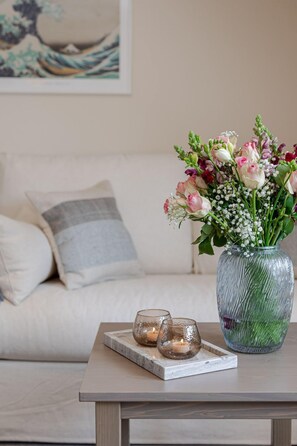 A living room with a sofa, a glass vase with flowers, and two lit candles on a tray. - Primera - Primera - charming maisonette in the heart of Keitum (Sylt)